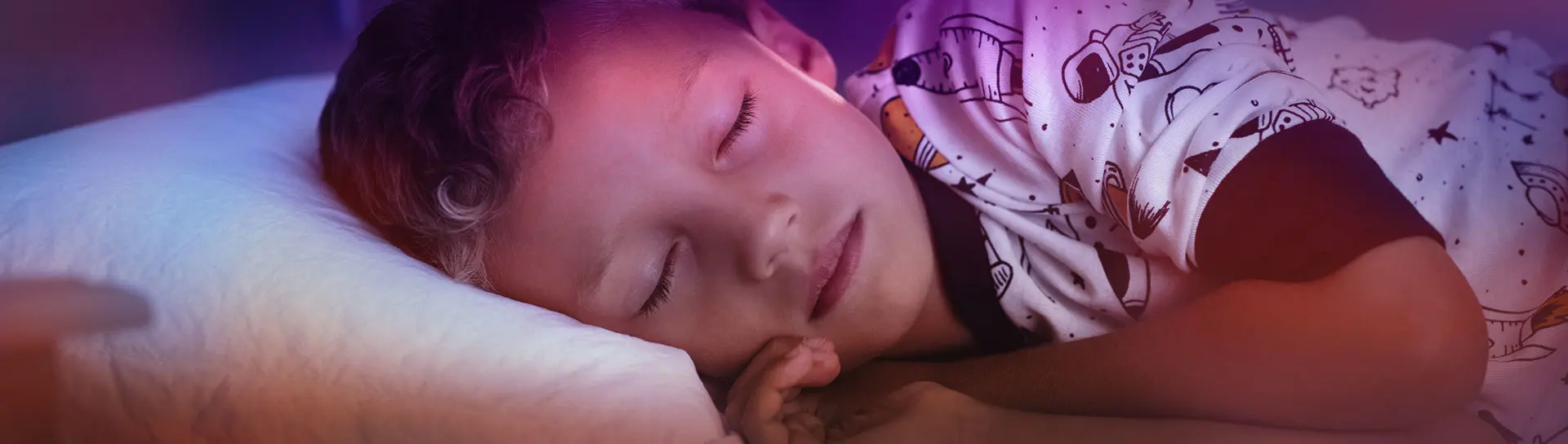 A little boy lying on side on bed and sleeping in bedroom decorated with planets and stars.