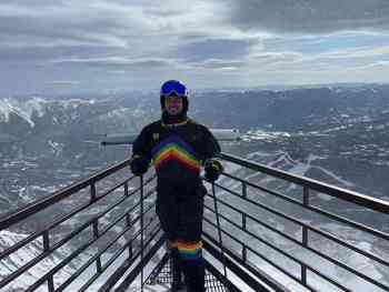 Taylor standing in full ski gear in front of a snowy mountain background