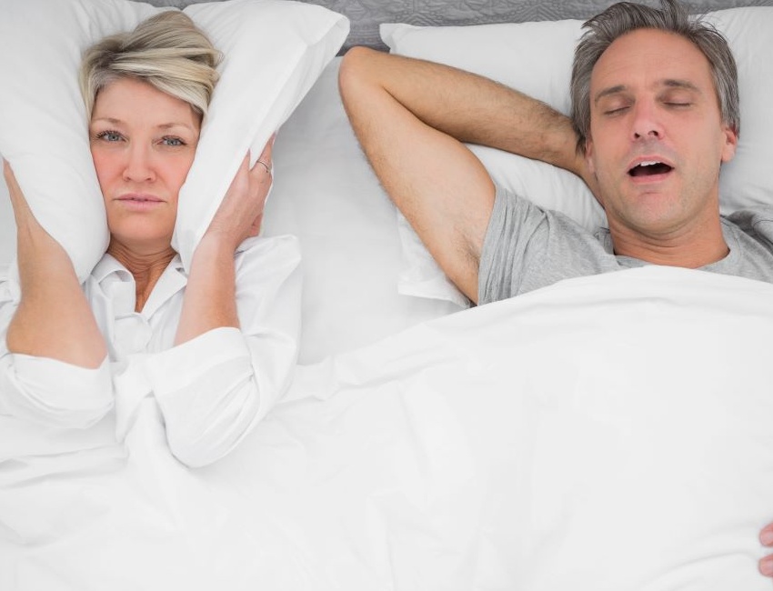 Woman using pillow to block snoring noise from man