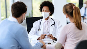 Female masked doctor talking to couple holding hands