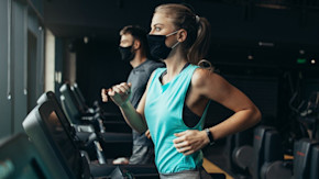 Masked woman and man running on treadmills