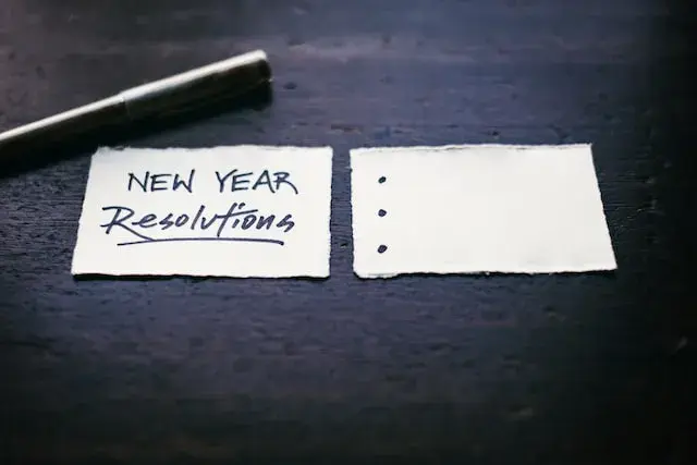 Paper reading “New Year Resolutions” with bullet points lays on a desk next to a pen.