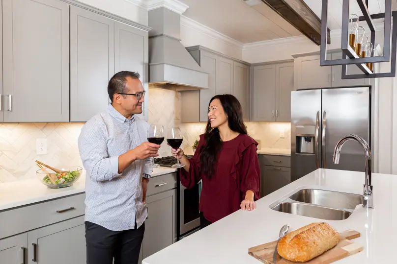 A couple in a kitchen holding wine glasses.