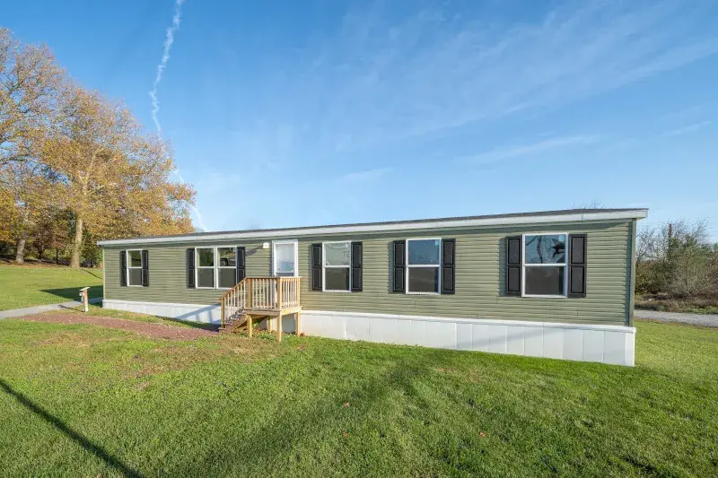 A green manufactured home on land on a sunny day.