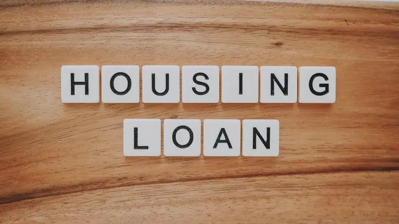 Scrabble letters that spell out housing loan against a wood background