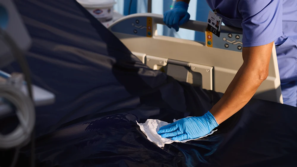 Person wearing a blue rubber glove wiping down a hospital bed