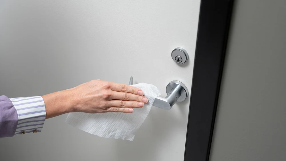 Hand wiping the handle of a door with a cleaning wipe