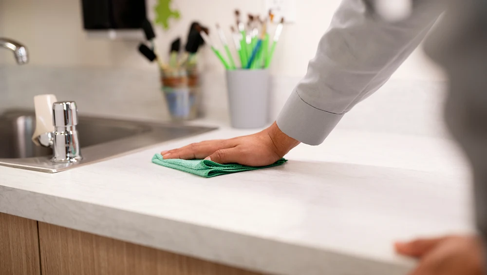 A person wiping a classroom sink counter with a green towel