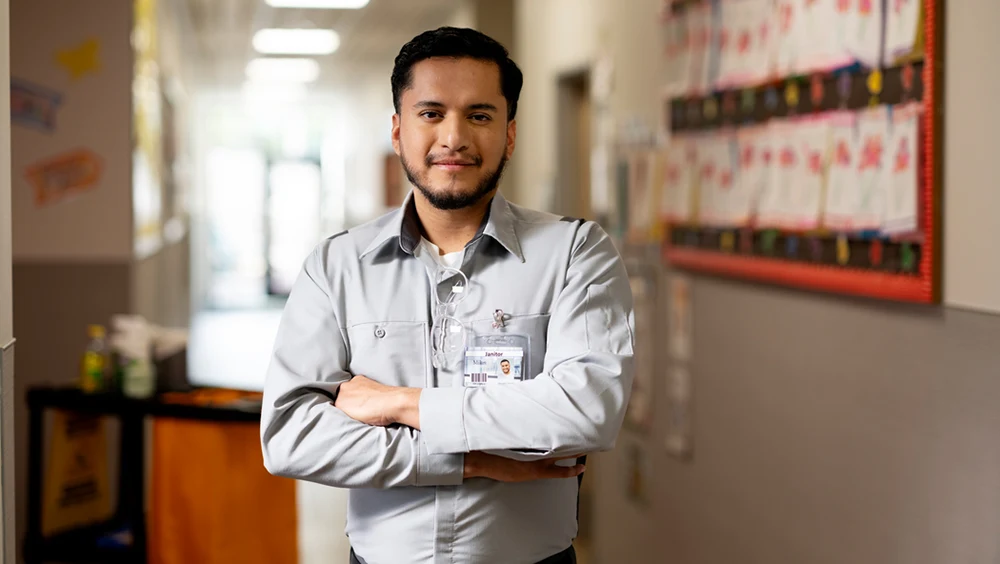 A janitor with his arms folded, standing in a hallway