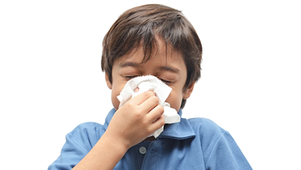 Child covering nose with a tissue while sneezing during cold and flu season.