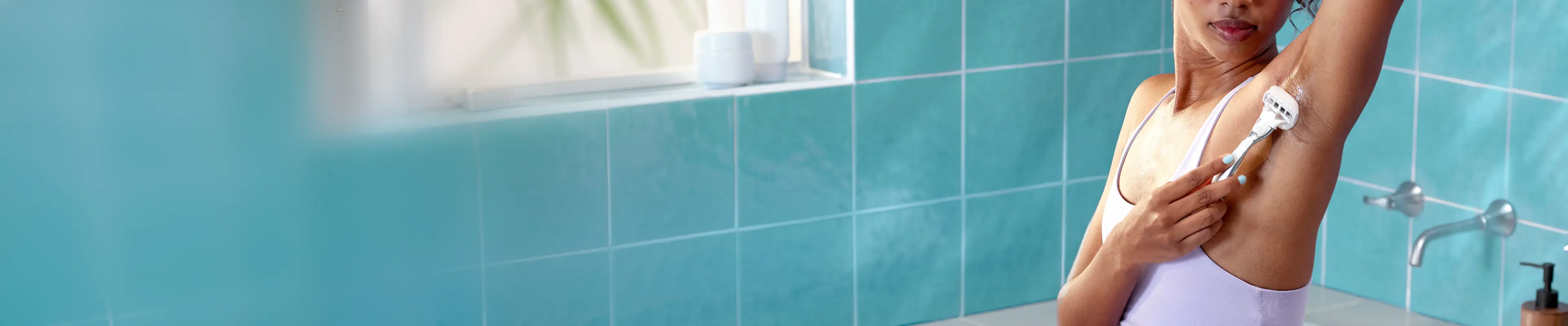 Femme se rasant les aisselles dans la salle de bain, démontrant une technique de rasage appropriée et des soins de la peau dans un environnement lumineux.