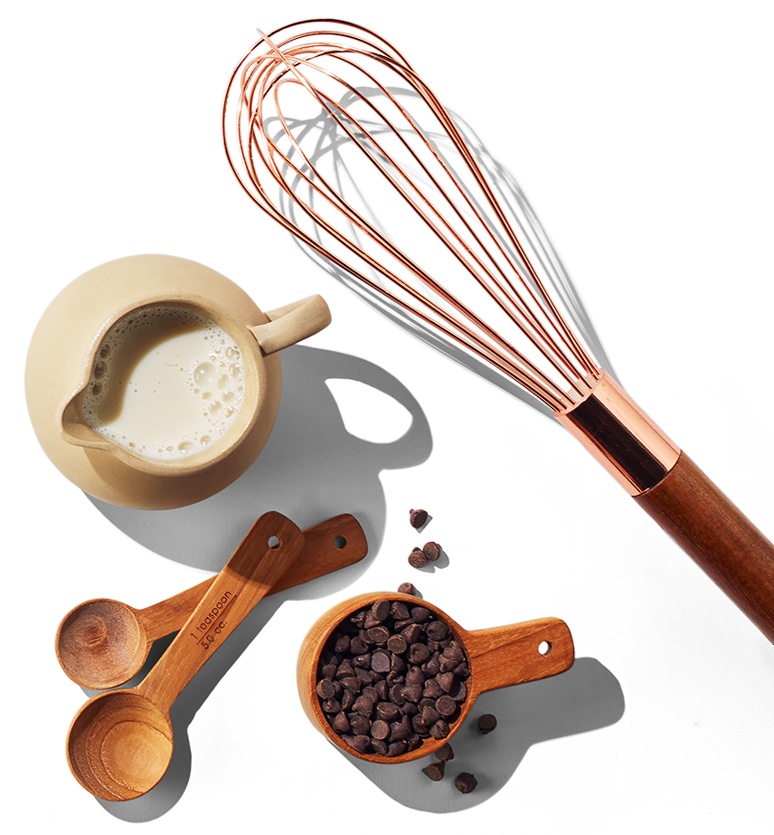 Un fouet, une tasse et des cuillères à mesurer en bois et un pot à lait.