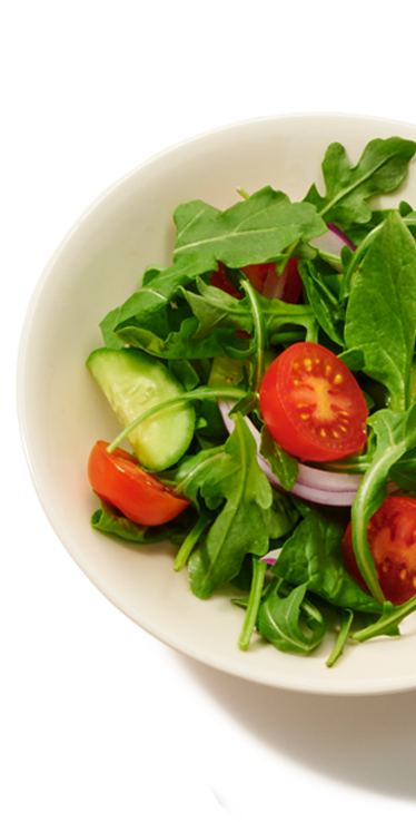A small individual dish containing a serving of salad containing greens, tomatoes, cucumbers and red onion
