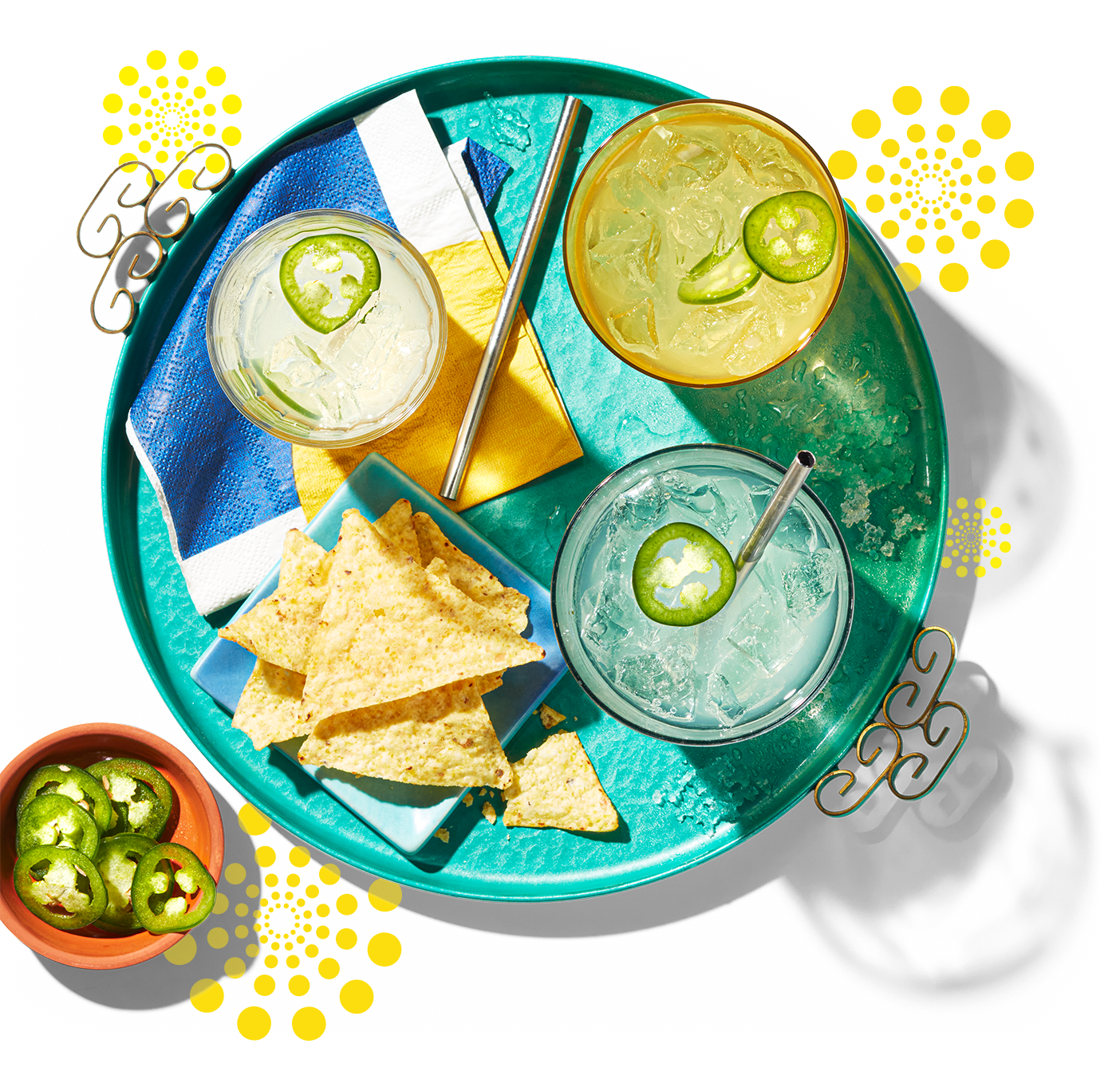 A round tray with an overhead view of three glasses of sparkling beverages garnished with slices of jalapenos and some tortillas on the side.