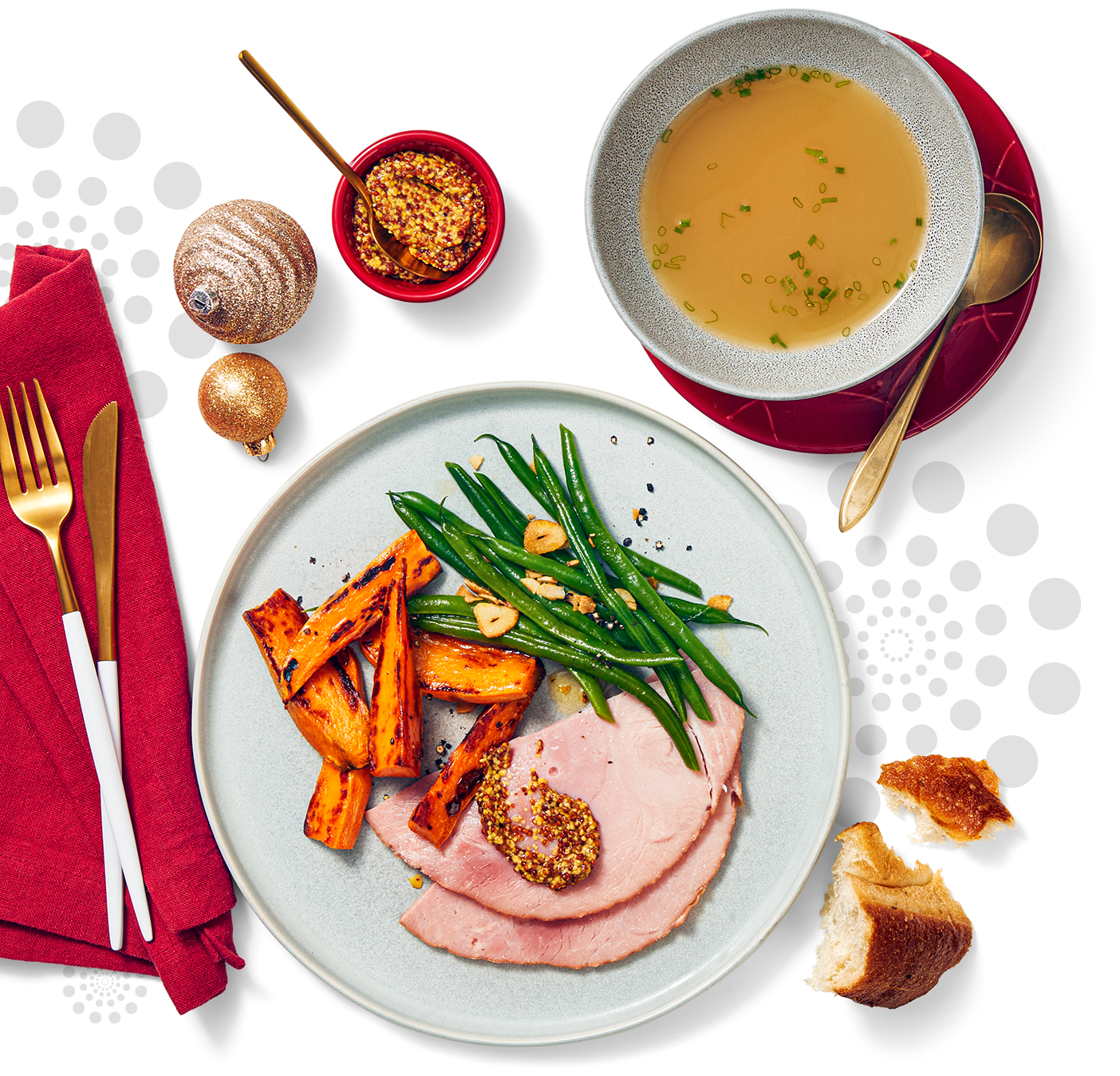 A charging plate with a healthy holiday serving of ham string beans and candied yam slices alongside is a bowl of soup and decorated with a few Christmas ornaments