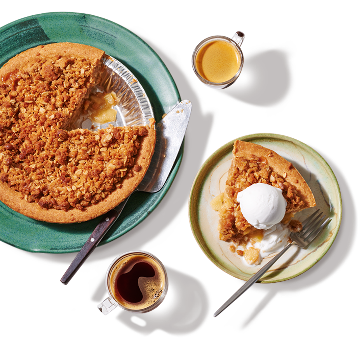 A Plant-based apple crumble ready to be served with one piece removed plated and served a la mode on with 2 hot beverages.