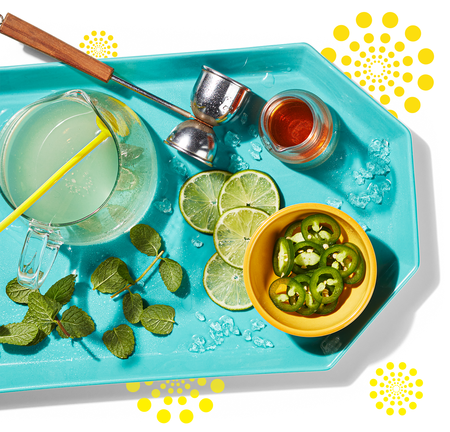 Une boisson pétillante à la limonade à côté de tranches de jalapeno, de tranches de lime et de feuilles de menthe sur un plateau.