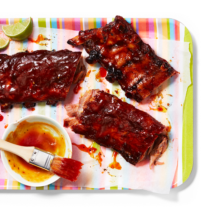 A Tray with 3 sectioned barbecue ribs with barbecue sauce and basting brush on the side.