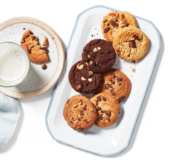 Assortiment de biscuits aux pépites de chocolat, aux brisures de chocolat et inverse Le Décadent PC sur un plateau entouré d'une assiette avec un biscuit à moitié mangé et d'un verre de lait.