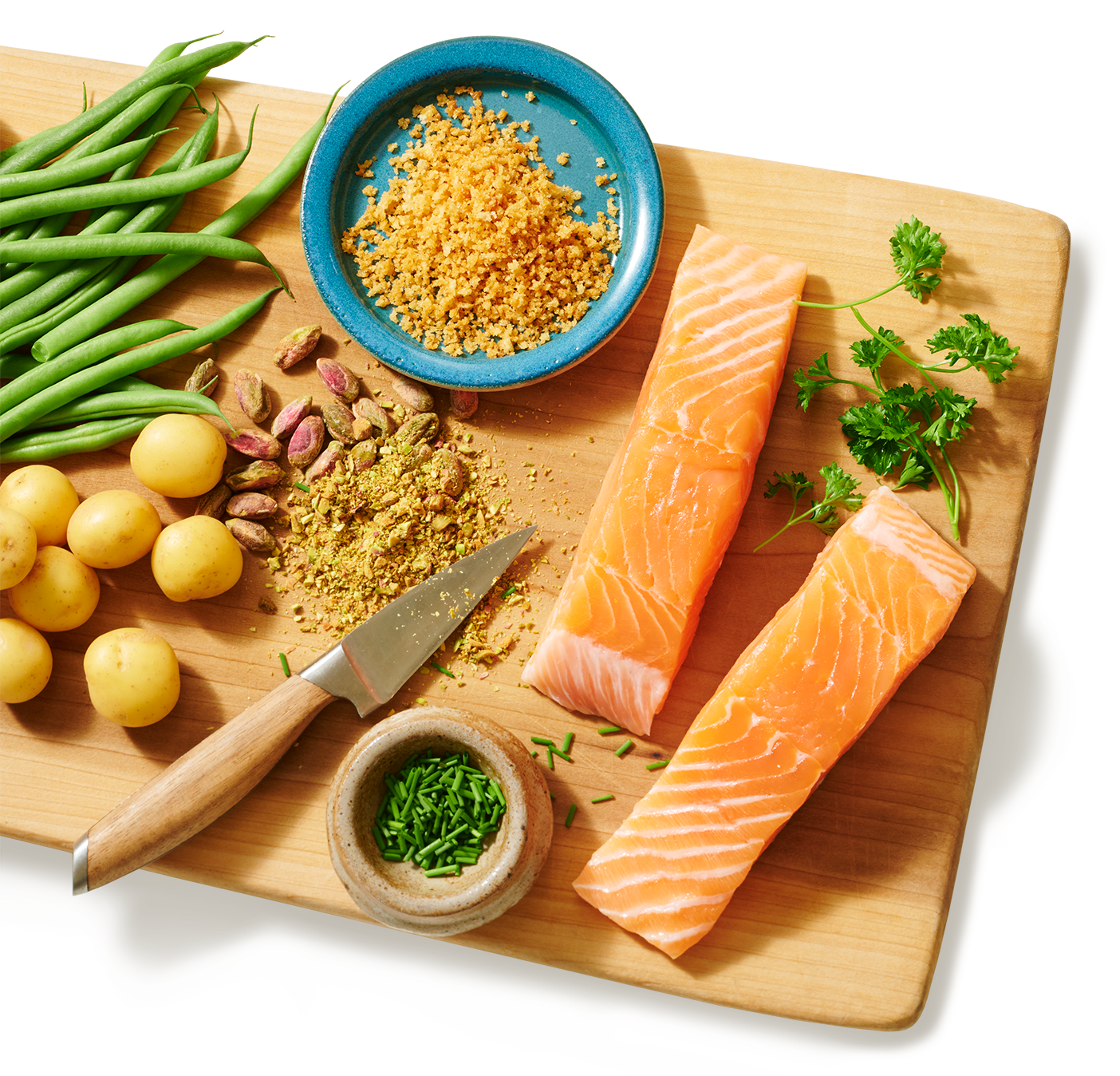 Une planche à découper sur laquelle sont posés deux morceaux de saumon prêts à cuire, à côté de haricots frais, de pommes de terre et d’assaisonnements