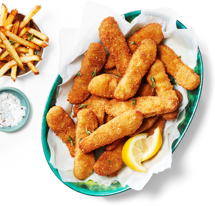 Un plat oval contenant des lanières sans poulet à base de plantes et des quartiers de citron, accompagnés d'une petite portion de frites dans un autre plat.