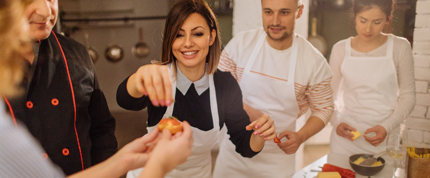 Une photo d'une jeune femme qui prépare une bruschetta dans une cuisine pendant un cours de cuisine.