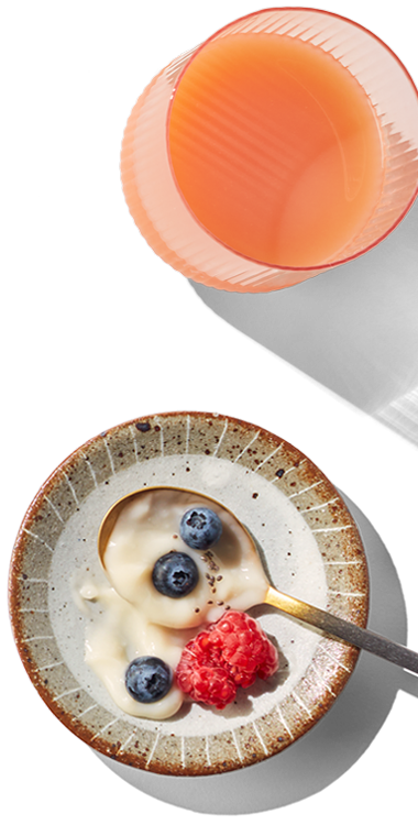 A small bowl of strawberries and blueberries. Another small bowl with a serving of plant based yogurt with a few berries and a glass of orange juice.