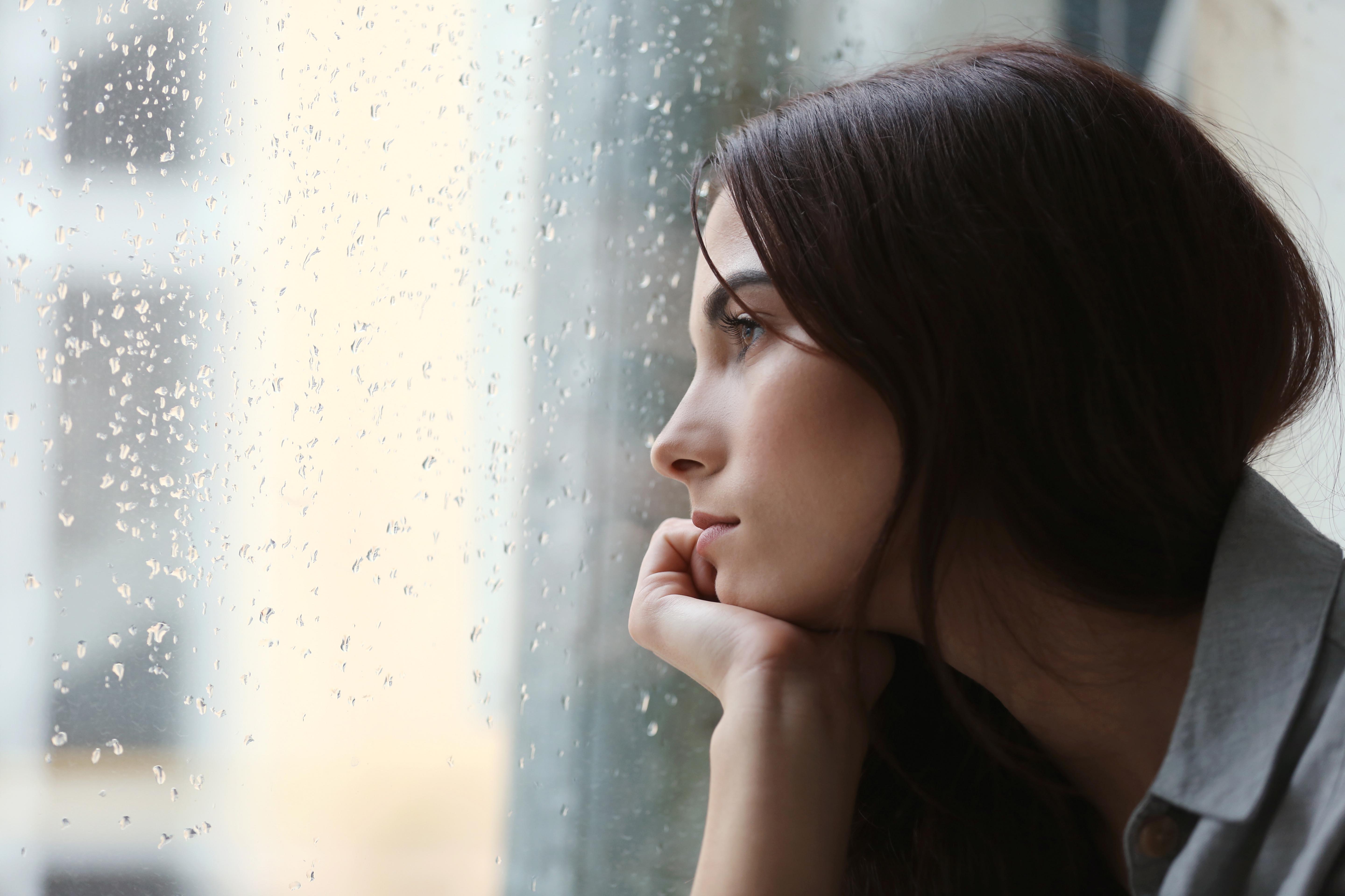 Yağmurlu günde pencereden bakan üzgün genç kız