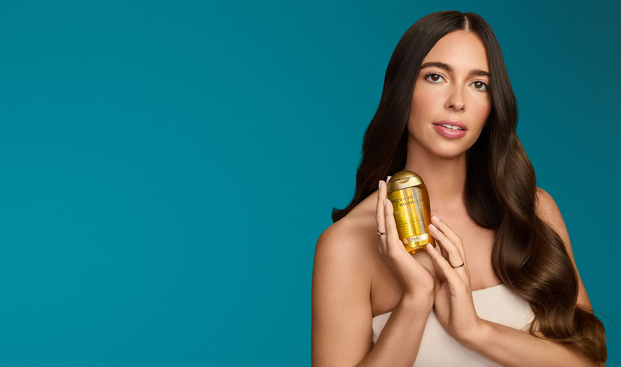 Woman with shiny hair holding OGX® Argan Oil of Morocco Penetrating Oil