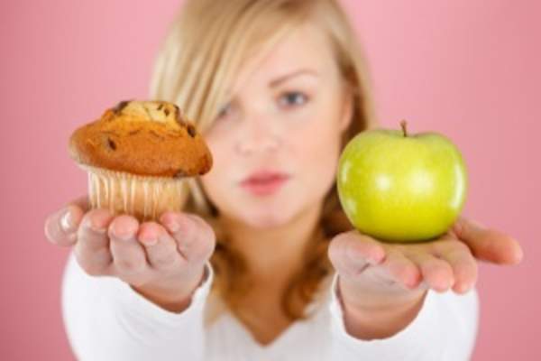 Woman choosing between muffin and apple image.