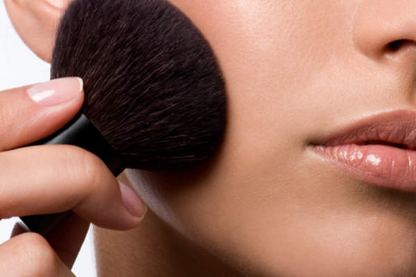 Women applying makeup to cheek with brush.