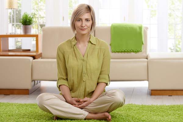 Happy woman sitting on carpet in her living room.