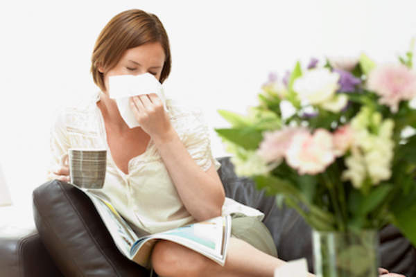 Woman sitting on couch, blowing nose in tissue.