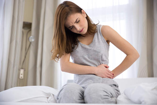 woman sitting on edge of bed clutching stomach in pain.
