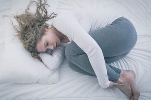 Young woman curled up in fetal position on bed