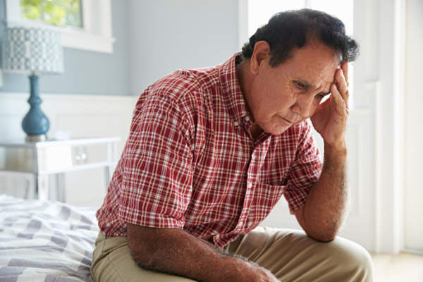 Senior man depressed and sitting on bed at home with head in hand.