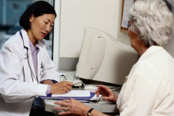 Elderly woman talking to doctor writing in medical history.