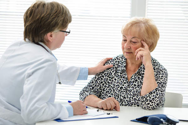 Doctor with hand on depressed senior woman's shoulder in support.