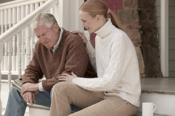 Adult daughter sitting with depressed father on the stairs at home.