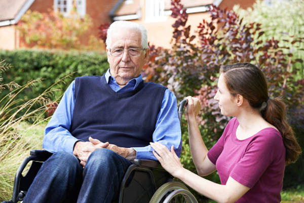 Senior father in wheelchair with adult daughter in garden.