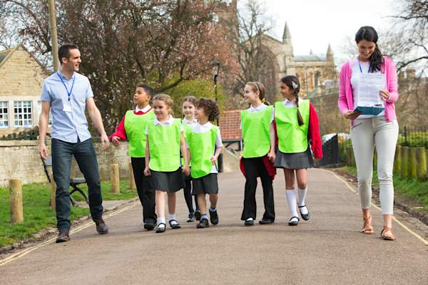 Adult and group of school children walking outside.