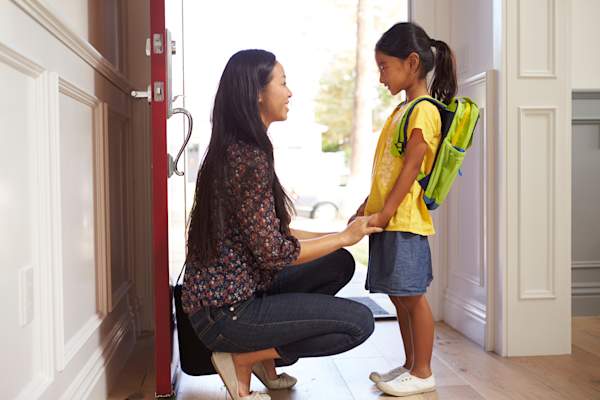 Mother and daughter with backpack in school hallway.