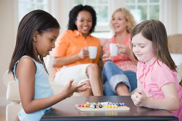 Mothers talking and having tea while their daughters play together.