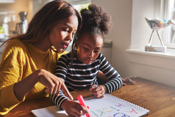 Mother helping her young daughter color a picture with markers.