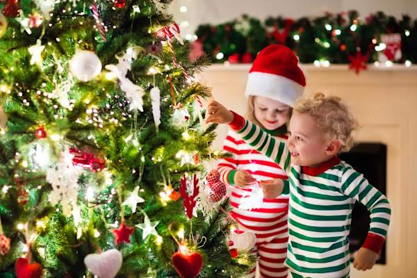Toddlers hanging ornaments on a Christmas tree.