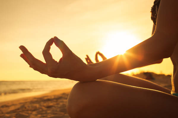 Woman meditating outside in the sunshine on the beach.