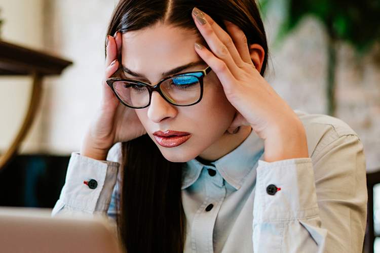 Young woman at her desk frowning at her laptop.