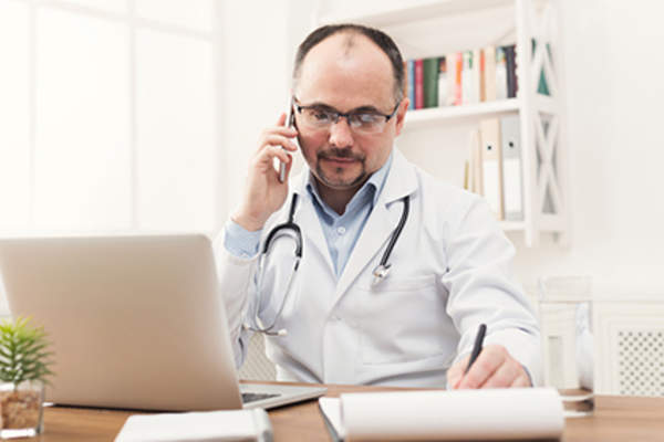 Doctor talking to patient on phone and taking notes.