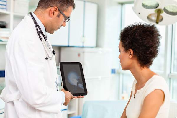 Doctor showing patient head and neck x-ray on tablet.