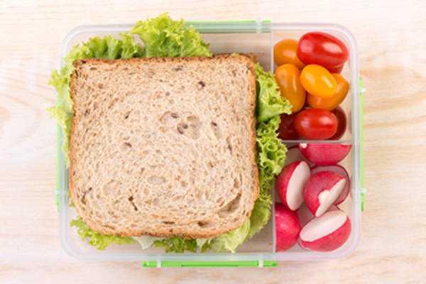 Sandwich and raw vegetables packed in plastic container.